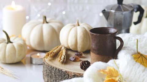 Pouring black coffee in a rustic cup with autumnal decorative pumpkins and burning candles at the background. Autumn blues or cozy autumn morning concept. Shallow depth of field