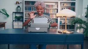 Funny video of smiling female writer, secretary or journalist typing text on retro typewriter while sitting in modern office. Concept for website and mobile development. African American woman typing.