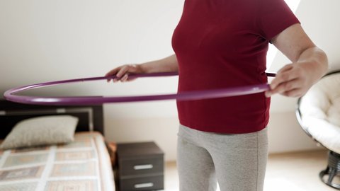 Close up of belly exercise with hula hoop, Overweight female in red t shirt twirling hula hoop, Fatty woman exercise for weight loss, slimming process. Slow motion.