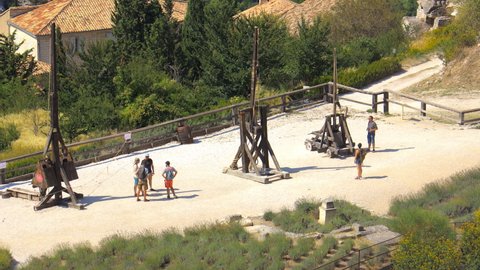 Les Baux-de-Provence, France - August 2021 :  Three old wooden catapults with some tourists visiting the castle of Les Baux de Provence 