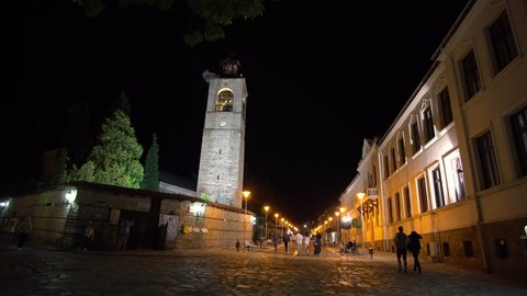 Bansko, Bulgaria - 20 Feb, 2020: People walk the old town street in the night with view of bell tower of church