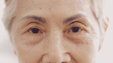 Face close up and 4K slow motion of asian senior lady who is 80 years old grandmother with high key style of bright background shows beautiful detail of wrinkle skin, black eyes and grey hairs.