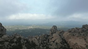 View from above, drone point of view, stunning aerial video of a drone flying over a granite mountain range during a cloudy day. San Pantaleo village in the distance, Sardinia, Italy.