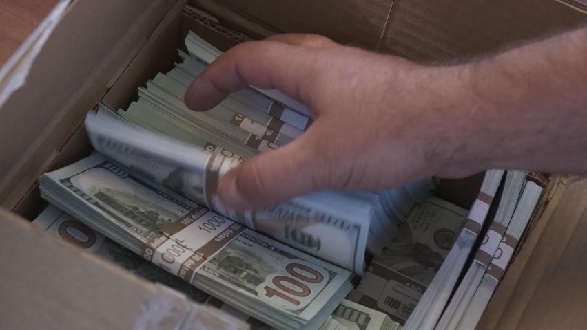 the man handles the bundles of money, packing the money in a cardboard box