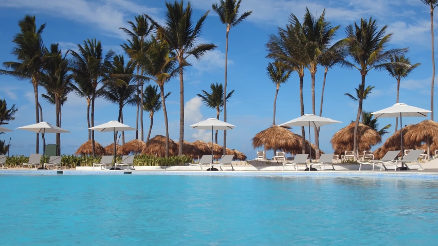 Pool with clear blue water, beach umbrellas and palm trees on the background. Amazing holidays in the all inclusive hotel  | Shutterstock HD Video #1079853740