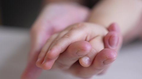 mom holds the hand of a newborn. close-up baby hand. hospital caring happy family medicine concept. baby newborn holding mom hand close-up indoor. mom takes care of the baby in the hospital
