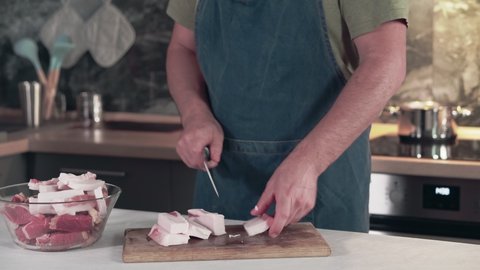 Man in an apron cuts lard with a knife. Slicing lard for cooking in the kitchen.