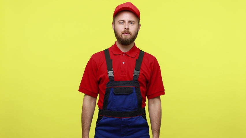 Extremely happy worker holding big american flag, yelling, celebrating national holiday, wearing blue uniform, red T-shirt and visor cap. Indoor studio shot isolated over yellow background.