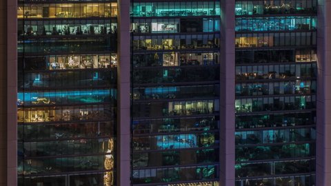 Big glowing windows in modern office buildings timelapse at night, in rows of windows light shines. People working inside and workers make a renovation