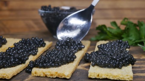 The cook puts black sturgeon caviar with a spoon on crispy rectangular rice slices. Dolly shot. An appetizer for those who love seafood