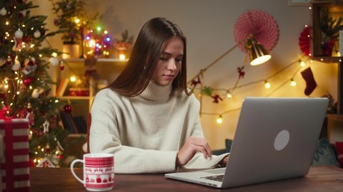 Woman typing on laptop computer close-up. Young student texting, sitting in decorated living room. Christmas holidays concept. Female person chatting with friends online, home office. 