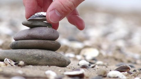 European male hand building stone stack at a river shore in tranquil atmosphere with calm movement of fingers and pebbles shows zen like harmony and relaxation in nature and coast side stone pyramid