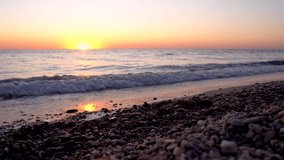4k video. Waves on the beach with pebbles at sunset, the sun goes into the water. The concept of feeling calm and zen