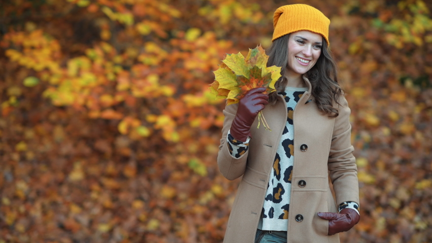 Hello autumn. happy young female in brown coat and yellow hat with autumn yellow leaves outdoors in the city park in autumn.