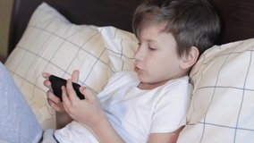 7 years old kid using gadget while laying in bed. Talking with friend on smartphone, close up