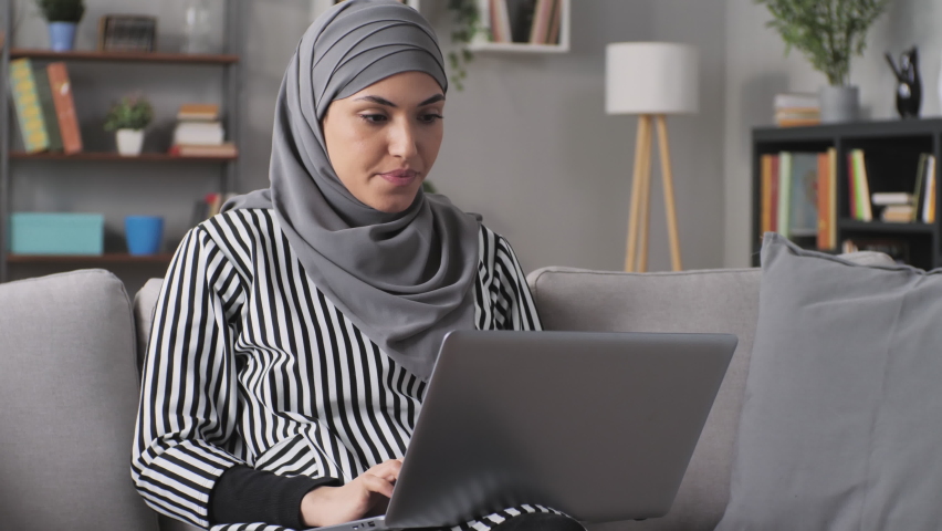 Furious stressed muslim woman working at the laptop has a burst of anger,hits her hands on the keyboard,overwhelmed angry arab female sits on couch using computer has a rage attack | Shutterstock HD Video #1079870939
