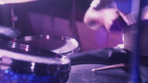 A professional male artist plays a drum kit. Night show in a musical instrument recording studio. The drummer knocks and beats, Repetition of rock or metal music band. Music party with colored lights