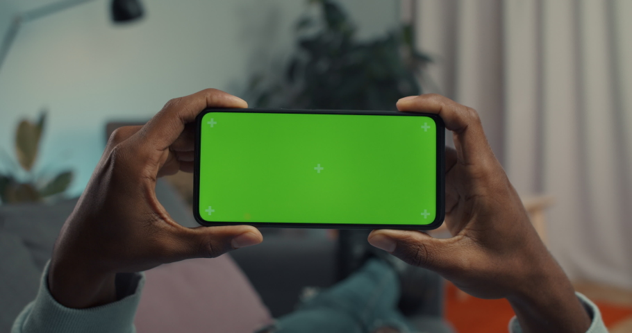 African american guy holding smartphone in horizontal position with green mock up screen. Focus on modern gadgets in male hands. Copy space. Royalty-Free Stock Footage #1079871257