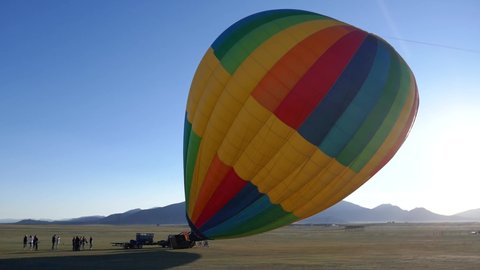 Rainbow colored hot air balloon getting inflated with bright morning daylight