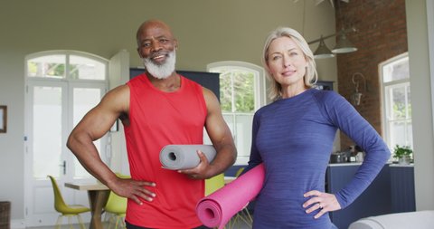 Senior couple holding yoga mat smiling at home. 