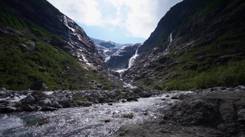 Steady shot of a Norwegian glacier river, melting ice builds rivers and Waterfalls. Glacier in the background