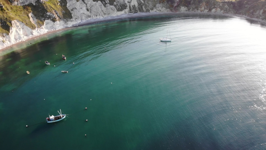 Boats Moored In Tranquil Turquoise Waters At Lulworth Cove. Aerial Dolly Forward
