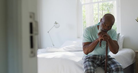 Thoughtful senior african american man in bedroom holding walking cane. retirement lifestyle, spending time at home.