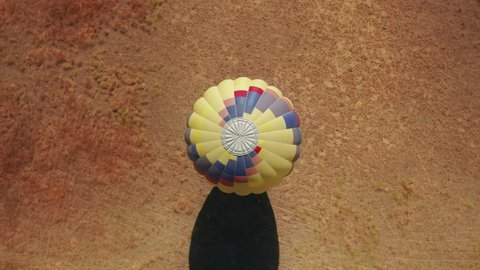 Aerial 4K top down view of landed vibrant colorful hot air balloon with tourists visiting sunny summer California, USA. Countryside landscape with dry field on motion background