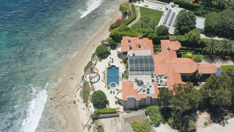 Malibu coast June 2020, California, USA. Ocean front private luxury villa with swimming pool and palms facing white sandy beach. Aerial 4K waterfront prestige real estate property Los Angeles suburban