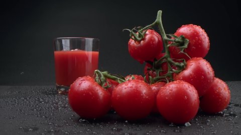 beautiful bunch of tomatoes and a glass into which tomato juice is poured on a black background. Tomatoes, washed and ready to juice