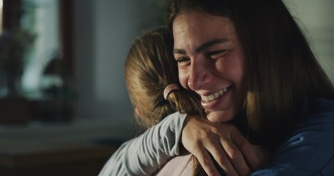 Cinematic authentic close up shot of happy smiling little daughter is giving affective hug to her mother while enjoying their time together in kitchen at home.