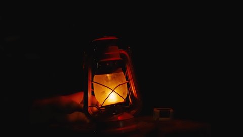 A man's hand twists the wick on a kerosene lamp and it slowly goes out. Halloween Concept