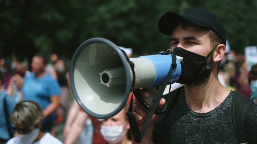 Political strike demonstration rebel guy in Covid-19 restrictions with bullhorn megaphone. Riot demonstrator activist in face mask on opposition resistance protest under lockdown. Rally revolt crowd. Royalty-Free Stock Footage #1079886620