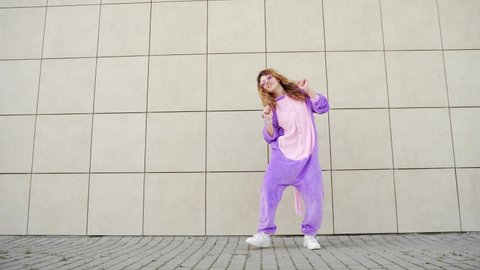 Funny cheerful happy young woman dancing outdoors on yellow wall. Crazy female hipster girl in a dress unicorn costume mask dance. Concept of fun people, happiness, joy Modern lifestyle in city street