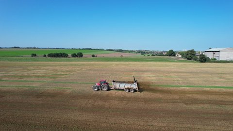 Organic fertilizer. A tractor with a trailer-spreader spreads cow dung in a field. View from the drone.