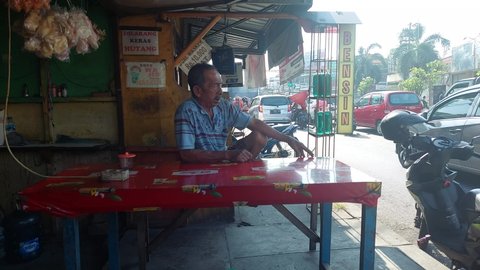Sidoarjo, Indonesia - September 28, 2021 : an old man sitting in a coffee shop at a red table smoking