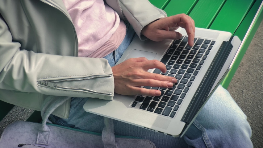 A female freelancer works on laptop in the park. Freelancing outdoor. Work and travel Concept.