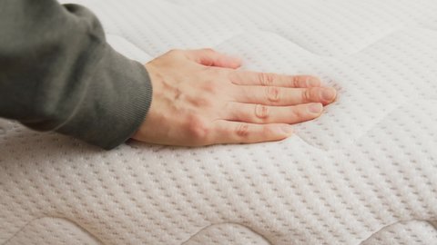 Hand touching and pressing orthopedic mattress on bed.
