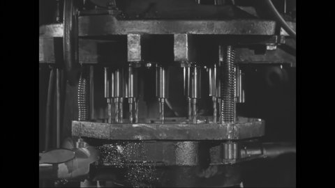 1930s: Two workers take a rear axle housing and lock it in place in a drill press. One worker turns a wheel to lower the drills. As the holes are being cut, the two workers ready the next axle.