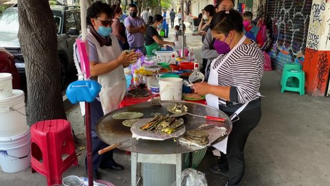 Mexico City, Mexico - September 25, 2021: Women, wearing face masks to protect from COVID-19 pandemic, prepare quesadillas and tlacoyos made with green tortillas in a street stall in Roma district.
