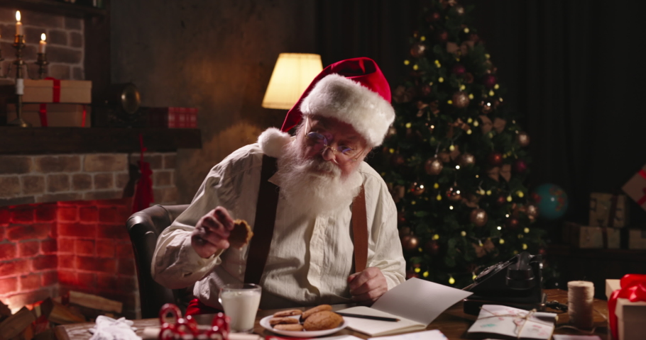 Santa Claus eating ginger cookies having break close-up. Mr Claus free time, relaxing after work, receiving letters, sitting at workplace in cozy house residence. Post office of Santa, leisure. | Shutterstock HD Video #1079913629
