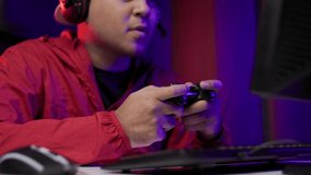 Close up male hands holding joystick game console. Young man playing video game online. Man in red jacket play computer pc at home in the dark room with neon light