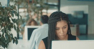 Portrait of young black business woman sitting in work space, chatting to discussing communicating by video call colleagues in office. Female looking at computer on online conference. 4K slow motion