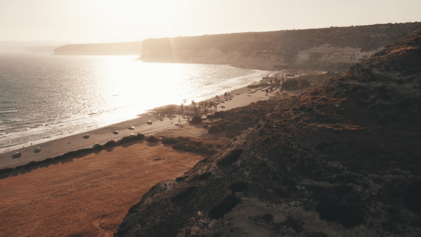 Orange sunset on mountain sea coast beach. Sun shine over fields farm plantations seashore, rocky highland landscape in countryside. Summer travel holiday vacation at seaside. Kourion beach, Cyprus.