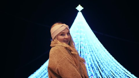 A girl poses against the background of a New Year tree in the evening in the city.