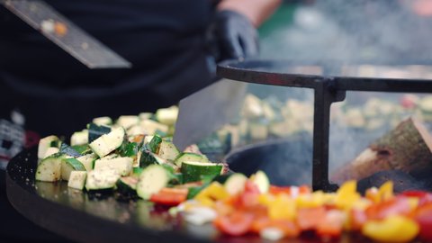 Close up shot of cut zucchini, onion, red and yellow bell peppers grilling on professional bbq smoker grid seasoned with aroma spices and herbs, process of preparation vegetables on bbq grill outdoor