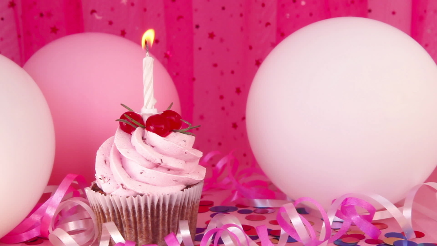Pink cupcake and white one candle on colorful background with air balloons, happy birthday and anniversary