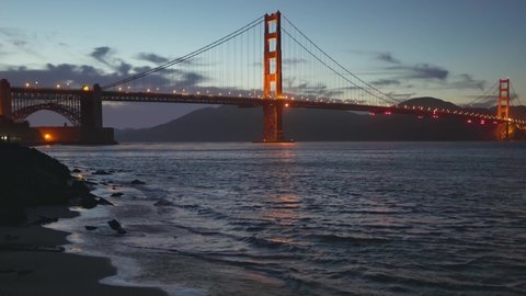 Zoom out shot of Golden Gate Bridge in evening time, view from the beach. San Francisco, United States