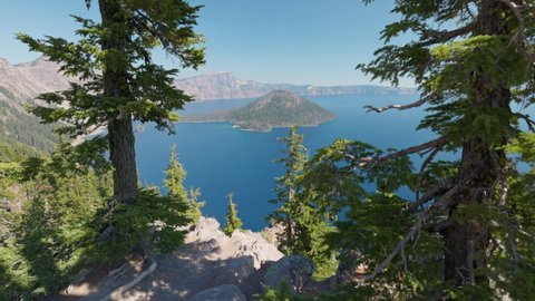 Crater Lake National Park, Oregon, USA. Camera moves between the tree trunks, view of the blue lake and the island. Gimbal shot, 4K