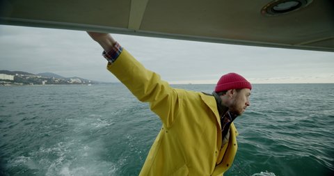 The fisherman is swiftly sailing on a boat in the open ocean. Handsome sailor in a yellow raincoat. Fishing in the sea.